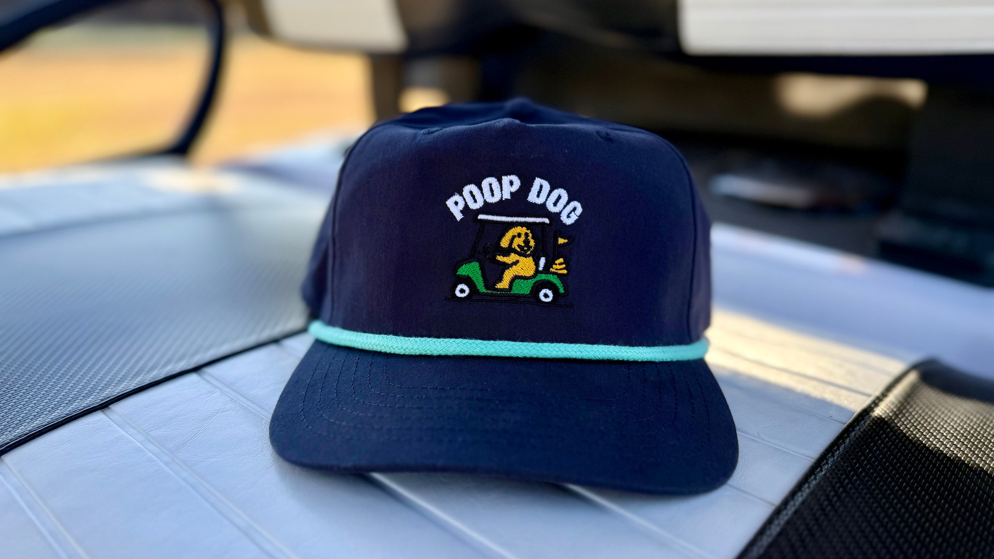 Navy blue cap with 'POOP DOG' text and graphic on a car dashboard.